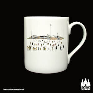 Könnte beinhalten: Weiße Keramiktasse mit einer Schwarzweißillustration eines Stadions mit Menschen auf den Tribünen. Der Text "Pirelli Stadium" ist auf einem Schild zu sehen.
