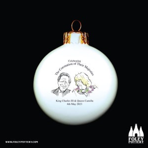 Puede incluir: Adorno navideño de cerámica blanca con parte superior dorada. El adorno presenta una ilustración en blanco y negro del rey Carlos III y la reina Camilla con el texto "Celebrating The Coronation of Their Majesties King Charles III & Queen Camilla 6th May 2023".