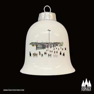 Könnte beinhalten: Weißer glockenförmiger Weihnachtsschmuck mit silberner Kappe und detaillierter Illustration. Die Illustration zeigt eine Straßenszene mit Menschen und Gebäuden. Der Schmuck trägt den Text "The Emporium" und "Foley Pottery".
