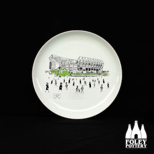 May include: A white ceramic plate with a black and white illustration of a stadium and people. The text "St. James' Park" is visible on the plate.