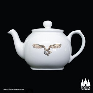 Puede incluir: Tetera de cerámica blanca con un diseño de búho de granero marrón y blanco. El búho está volando con las alas extendidas.