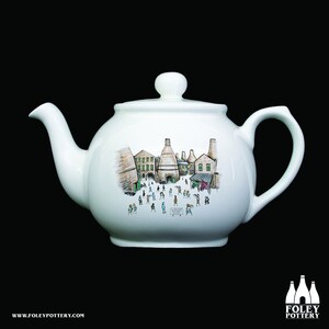 May include: White ceramic teapot with a hand-painted illustration of a brick building with chimneys and people walking around. The illustration is in shades of brown, green, and black.