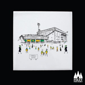 May include: A black and white illustration of a stadium with people walking towards it. The stadium has green and yellow flags hanging from it. A sign reads "Carrow Road".