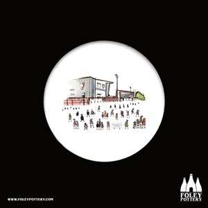 Puede incluir: Un posavasos de cerámica blanca con una ilustración dibujada a mano de un estadio con una multitud de personas delante. El estadio es gris y rojo con el texto "JERSEY" en el lateral. Las personas llevan camisas a rayas rojas y blancas. El texto "KINGSDOWN STADIUM" está en un cartel delante del estadio.