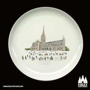 May include: White ceramic plate featuring a detailed illustration of Salisbury Cathedral, with tiny figures of people in the foreground. The plate has a glossy finish and the text "SALISBURY CATHEDRAL" is visible. The Foley Pottery logo is in the bottom right corner.