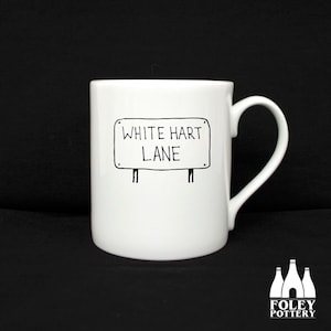 May include: White ceramic mug with a black and white illustration of a street sign that reads "White Hart Lane".