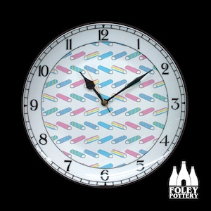 May include: A white ceramic clock with black numbers and hands. The clock face has a pattern of colorful, striped, candy-like shapes. The clock is made by Foley Pottery.