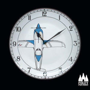 May include: A white ceramic clock face with black Roman numeral hour markers and black hands. The clock face features a blue and white airplane design in the center.