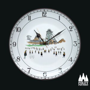May include: A white ceramic clock with black hands and a black rim. The clock face features a black and white illustration of a coal mine with a group of miners in yellow and black uniforms. The clock face also includes the text "WITCHAM COLLIERY".