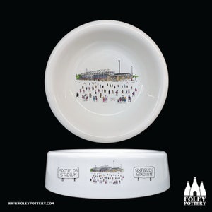Peut inclure: Bol en céramique blanche avec une illustration en noir et blanc d'un stade avec des gens autour. Le bol porte l'inscription "Sixfields Stadium" des deux côtés.