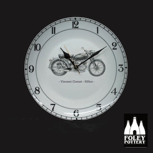 May include: White ceramic clock with black numbers and hands. The clock face features a black and white illustration of a Vincent Comet motorcycle with the text "Vincent Comet - 500cc -" below the motorcycle. The clock is made by Foley Pottery.