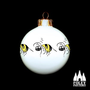 May include: White Christmas ornament with a black and yellow bee design. The bee is repeated multiple times around the ornament.