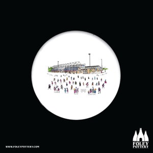 Peut inclure: Un dessous de verre en céramique blanche avec une illustration en noir et blanc d'un stade avec des personnes devant. Le stade a un panneau qui dit "Bienvenue".