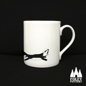 May include: White ceramic mug with a black and white illustration of a badger running. The mug has a handle on the right side. The mug is made by Foley Pottery.