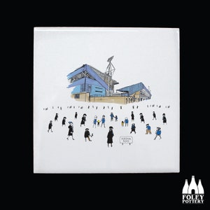 May include: A white ceramic tile with a black and white illustration of a stadium and people walking towards it. The stadium is blue and white and has a sign that says "Portiman Road".