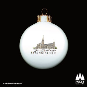 May include: White ceramic Christmas ornament with a hand-drawn illustration of a cathedral and people in front of it.
