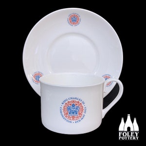 May include: White ceramic teacup and saucer set. The cup and saucer feature a circular emblem with a crown and the text "King Charles III Coronation 6th May 2023" in red and blue. The Foley Pottery logo is in the bottom right corner.