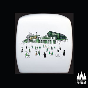 Puede incluir: Un azulejo de cerámica blanco con una ilustración dibujada a mano de un estadio verde y blanco con gente caminando hacia él. El texto "HOME PARK" es visible en un cartel.