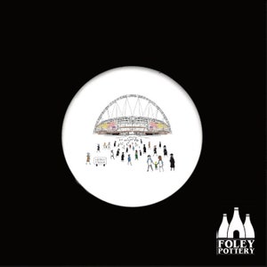 May include: A white ceramic coaster with a black and white illustration of Wembley Stadium and people walking towards it. The text "Wembley Stadium" is written on a sign in the bottom left corner of the image.