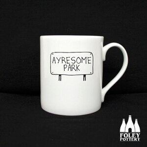 May include: White ceramic mug with a black line drawing of a sign that says "Ayresome Park".