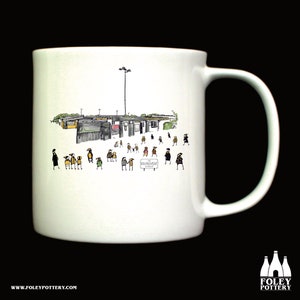Könnte beinhalten: Weiße Keramiktasse mit einer Schwarzweißillustration eines Schulgebäudes und Menschen, die darauf zugehen. Der Text "The Environment" steht auf einem Schild vor dem Gebäude.