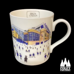 May include: White ceramic mug with a blue and yellow illustration of Ibrox Stadium, a football stadium in Glasgow, Scotland. The mug has the words "Ibrox Stadium" printed on the side. The mug is made by Foley Pottery.