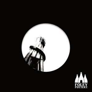 May include: Black and white photo of a tall, striped tower with a round top. The tower is seen through a circular opening in a black background. The text "FOLEY POTTERY" is at the bottom of the image.