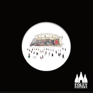 May include: A white ceramic coaster featuring a black and white illustration of a stadium with people in front of it. The stadium is labelled "St. Mary's Stadium".