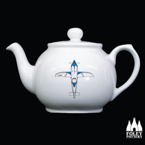 May include: White ceramic teapot with a blue and white airplane design. The teapot has a round body and a spout on the left side. The handle is on the right side.