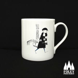 May include: White ceramic mug with a black and white illustration of a person wearing a scarf and walking past a building with a tall tower. The mug has a black handle and the words "FOLEY POTTERY" are printed on the bottom.