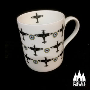 May include: White ceramic mug with a black and white pattern of fighter planes and red, white, and blue roundels. The mug has a handle and the text "FOLEY POTTERY" is printed on the bottom.