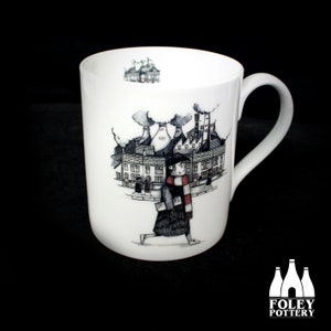 May include: White ceramic mug featuring a black and white illustration of a person walking past a factory. The person is wearing a red and white scarf. The mug has the words "FOLEY POTTERY" printed on the bottom.