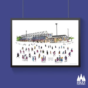 Peut inclure: Une affiche encadrée représentant le stade Sixfields, avec une foule de personnes. L'illustration colorée comprend le stade et une pancarte indiquant "Sixfields Stadium". L'affiche est accrochée à un mur bleu.