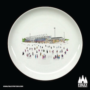 Peut inclure: Une assiette en céramique blanche avec une illustration en noir et blanc d'un stade avec des gens devant. Le texte "Notts Co Stadium" est visible sur le panneau.