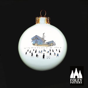 May include: White Christmas ornament with a blue and white illustration of a stadium and people walking towards it. The text "Goodison Park" is visible on a sign. The ornament is made by Foley Pottery.