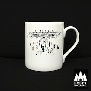 May include: White ceramic mug with a black and white illustration of a crowd of people walking towards Wembley Stadium. The mug has a black handle and the words "Wembley Stadium" are printed on a sign in the illustration.