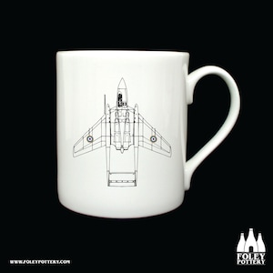 Könnte beinhalten: Eine weiße Keramiktasse mit einer schwarzen Linienzeichnung eines Vintage-Flugzeugs. Das Flugzeug ist ein De Havilland DH-106 Comet 1, ein britisches Düsenflugzeug. Das Flugzeug ist in Draufsicht dargestellt, mit ausgebreiteten Flügeln. Die Tasse hat einen schwarzen Henkel.