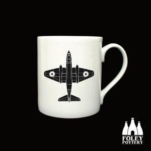 Könnte beinhalten: Eine weiße Keramiktasse mit einer schwarzen Silhouette eines Vintage-Flugzeugs. Die Tasse hat einen Henkel auf der rechten Seite.