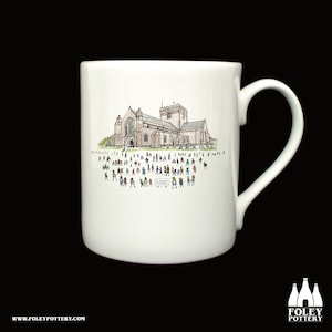 Puede incluir: Taza de cerámica blanca con una ilustración en blanco y negro de una iglesia con una multitud de personas delante. El texto "St. Agatha's Church" es visible en un cartel delante de la iglesia.