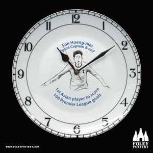 May include: A white ceramic clock with black numbers and hands. The clock features a black and white illustration of Son Heung-min, a football player, with the text "Son Hueng-min Spurs Captain & no7 1st Asian player to score 100 Premier League goals".