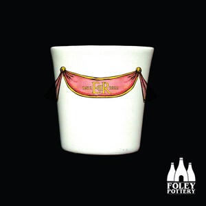 May include: White ceramic mug with a red and gold banner that says "1952 ER 2022". The mug is made by Foley Pottery.