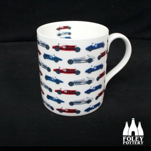 Puede incluir: Taza de cerámica blanca con un patrón de coches de carreras vintage azules y rojos. La taza tiene un asa y dice "FOLEY POTTERY" en la parte inferior.