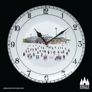 Peut inclure: Une horloge en céramique blanche avec des chiffres et des aiguilles noirs. Le cadran de l'horloge présente une illustration en noir et blanc d'un stade avec des personnes au premier plan. Le texte "SOTELDS STROIUPT" est visible sur le cadran de l'horloge.