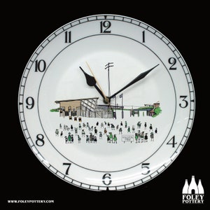 May include: A white ceramic clock with black numbers and hands. The clock face features a black and white illustration of a sports stadium with people in the stands. The text "KINGSTON PARK" is visible on the clock face.