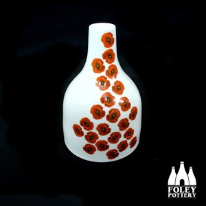 Pode incluir: Vaso de cerâmica branca com um design de flores de papoula laranja. O vaso tem uma base larga e um pescoço estreito.