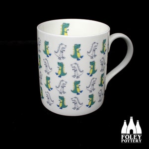 May include: White ceramic mug with a repeating pattern of green and white dinosaurs. The mug has a handle and the text "FOLEY POTTERY" is printed on the bottom.