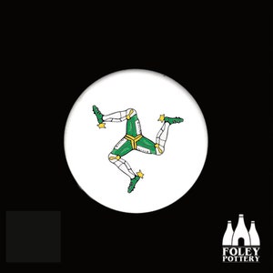 May include: White ceramic coaster with a green, white, and yellow three-legged symbol, the Isle of Man flag.
