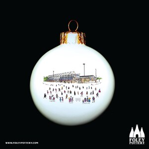 Puede incluir: Adorno navideño blanco con una ilustración dibujada a mano de un estadio con personas en primer plano. El adorno tiene una parte superior dorada y un fondo blanco.