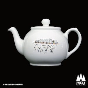 May include: White ceramic teapot with a black and white illustration of a stadium with people in the stands. The teapot has a black handle and spout.
