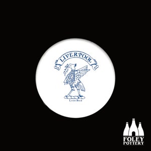 Puede incluir: Posavasos de cerámica blanca con una imagen azul y blanca del Liver Bird, el símbolo de Liverpool, Inglaterra. El texto "Liverpool" está escrito en una pancarta sobre el pájaro. El texto "Liver Bird" está escrito debajo del pájaro.